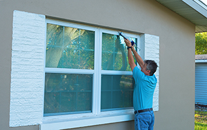 homeowner caulking windows before a storm